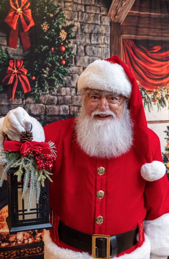 Santa Roger holding a lit lantern and smiling at the camera