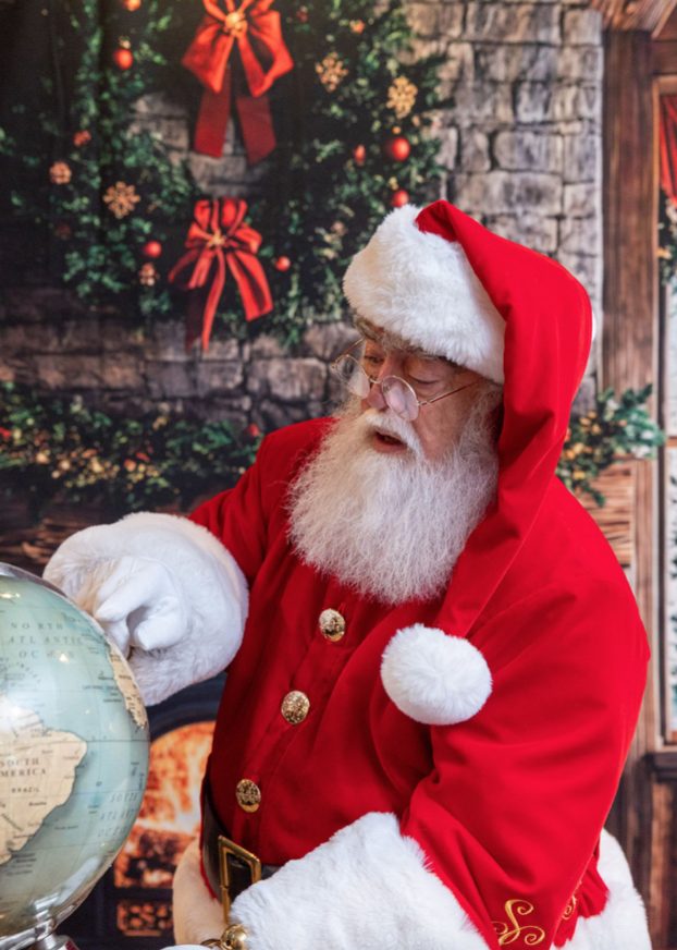 Santa Roger studying a globe, planning the Christmas Eve route